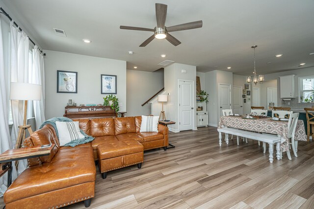 living room featuring ceiling fan with notable chandelier and light hardwood / wood-style flooring