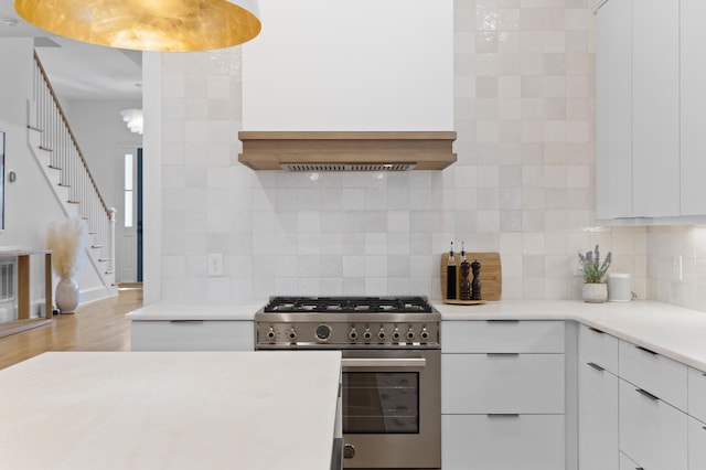 kitchen with light countertops, stainless steel stove, white cabinets, and backsplash