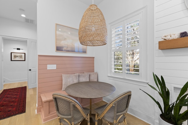 dining room featuring visible vents, baseboards, breakfast area, wood walls, and light wood-style floors