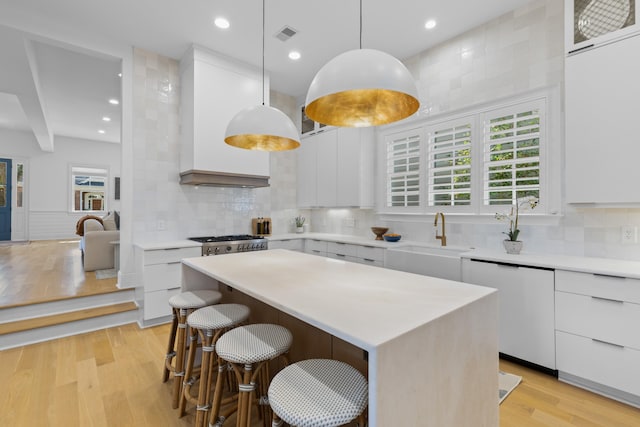 kitchen featuring white cabinets, a center island, light countertops, pendant lighting, and a sink