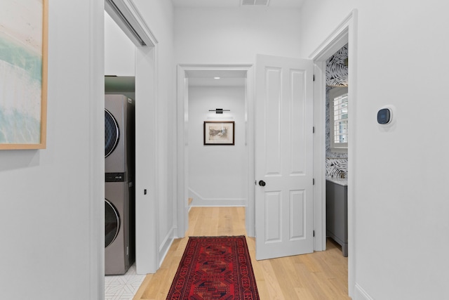 hall featuring visible vents, baseboards, light wood-style flooring, and stacked washer / drying machine