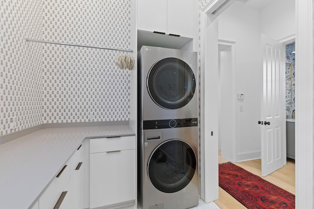 laundry area featuring light wood finished floors, stacked washer / dryer, and cabinet space