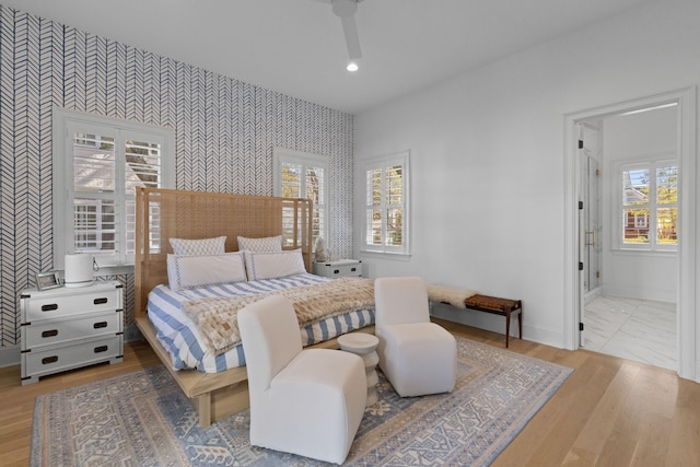 bedroom featuring an accent wall, wood finished floors, baseboards, and wallpapered walls