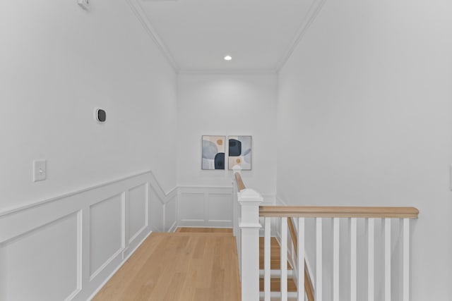 hall with crown molding, light wood finished floors, recessed lighting, a decorative wall, and an upstairs landing