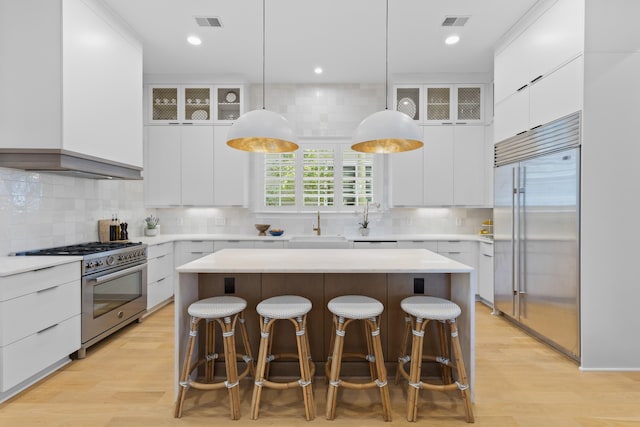 kitchen featuring white cabinets, high quality appliances, light countertops, and a center island