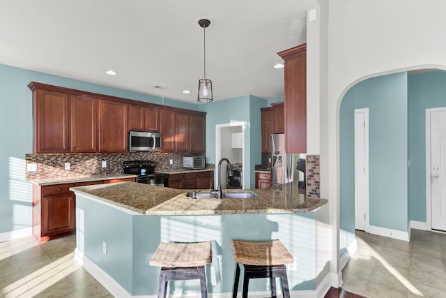 kitchen featuring light stone countertops, appliances with stainless steel finishes, a peninsula, arched walkways, and a sink