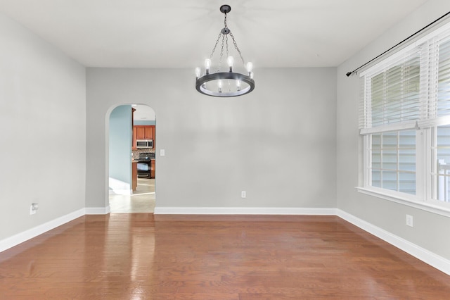 unfurnished room featuring arched walkways, an inviting chandelier, light wood finished floors, and baseboards