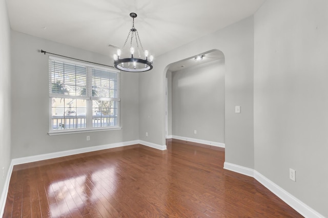 unfurnished room featuring baseboards, arched walkways, an inviting chandelier, and dark wood finished floors