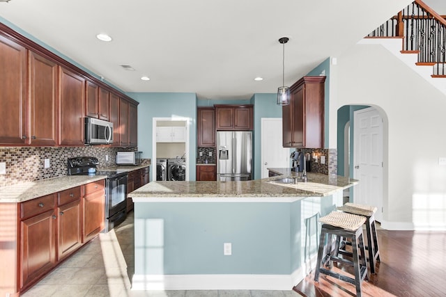 kitchen with a sink, stainless steel appliances, arched walkways, separate washer and dryer, and a peninsula