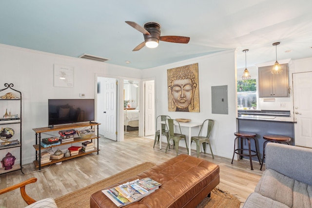 living room with electric panel, ceiling fan, ornamental molding, and light wood-type flooring