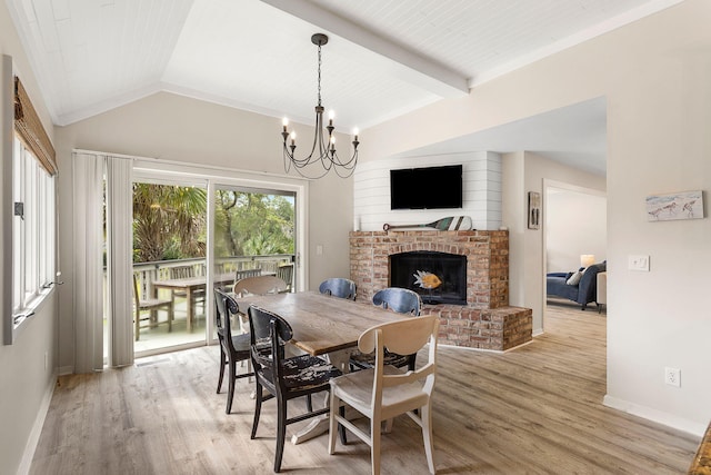 dining area featuring baseboards, vaulted ceiling with beams, light wood-type flooring, a fireplace, and a notable chandelier