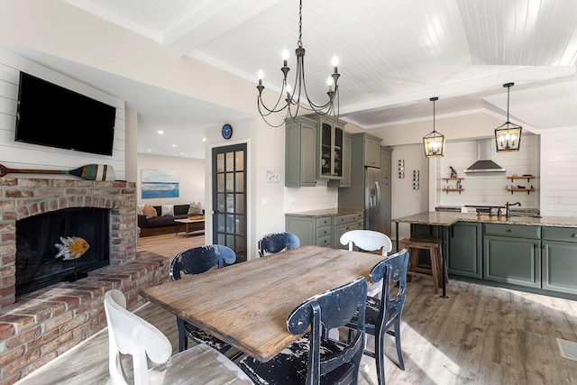 dining area with visible vents, light wood-style flooring, vaulted ceiling with beams, a brick fireplace, and a chandelier