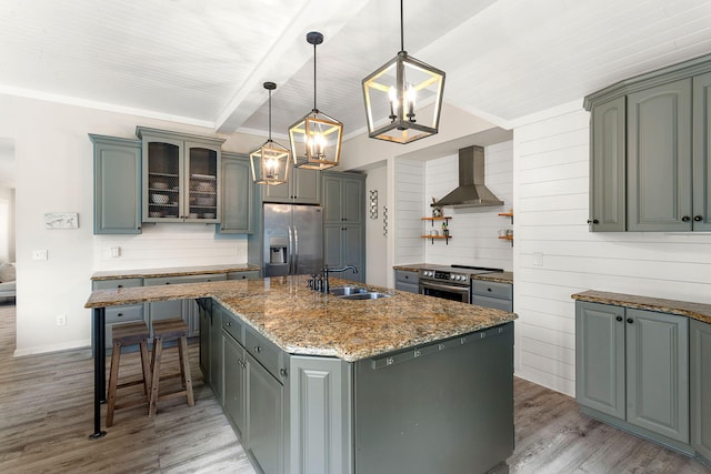 kitchen with stainless steel appliances, light wood-style floors, a kitchen island with sink, a sink, and wall chimney exhaust hood