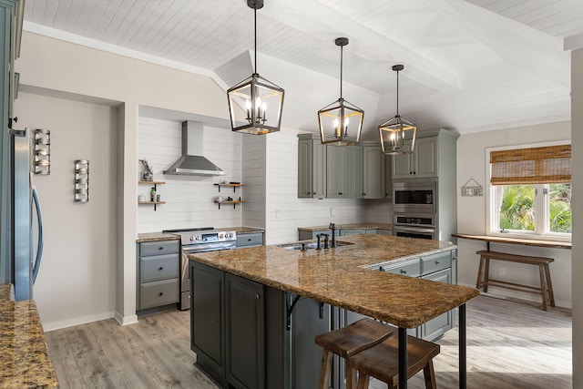 kitchen with wall chimney range hood, gray cabinets, a sink, and appliances with stainless steel finishes