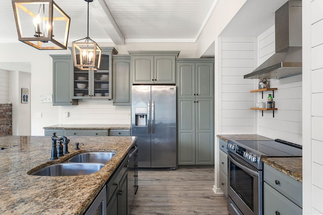 kitchen with appliances with stainless steel finishes, dark stone countertops, wood finished floors, wall chimney range hood, and a sink