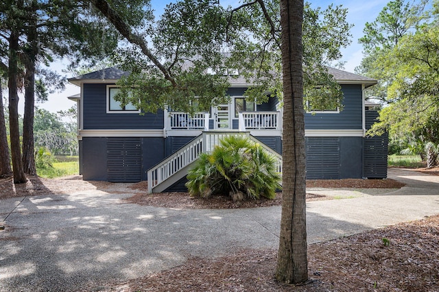 coastal home featuring covered porch, driveway, a shingled roof, and stairway