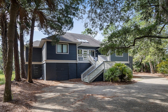 raised beach house with driveway, stairway, and roof with shingles