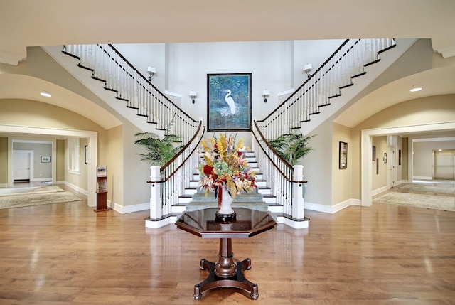 foyer entrance featuring a towering ceiling, stairs, baseboards, and wood finished floors