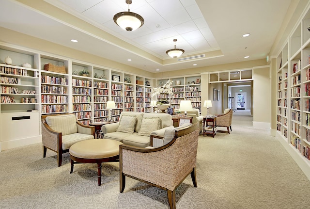 sitting room with visible vents, ornamental molding, carpet, a raised ceiling, and wall of books