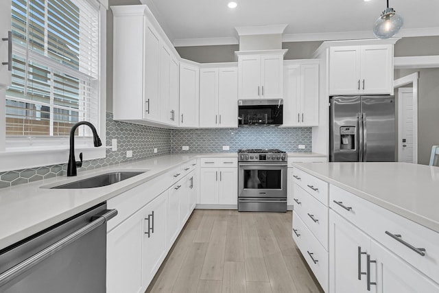 kitchen featuring hanging light fixtures, white cabinetry, appliances with stainless steel finishes, ornamental molding, and sink