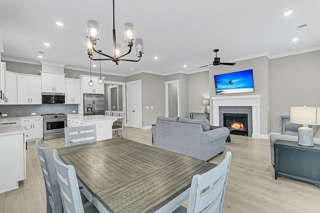 dining space featuring ornamental molding, ceiling fan with notable chandelier, light hardwood / wood-style flooring, and a fireplace