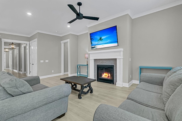 living room with a brick fireplace, ceiling fan, light hardwood / wood-style floors, and crown molding