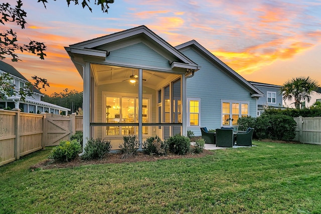 back house at dusk featuring a patio area, ceiling fan, a lawn, and a sunroom