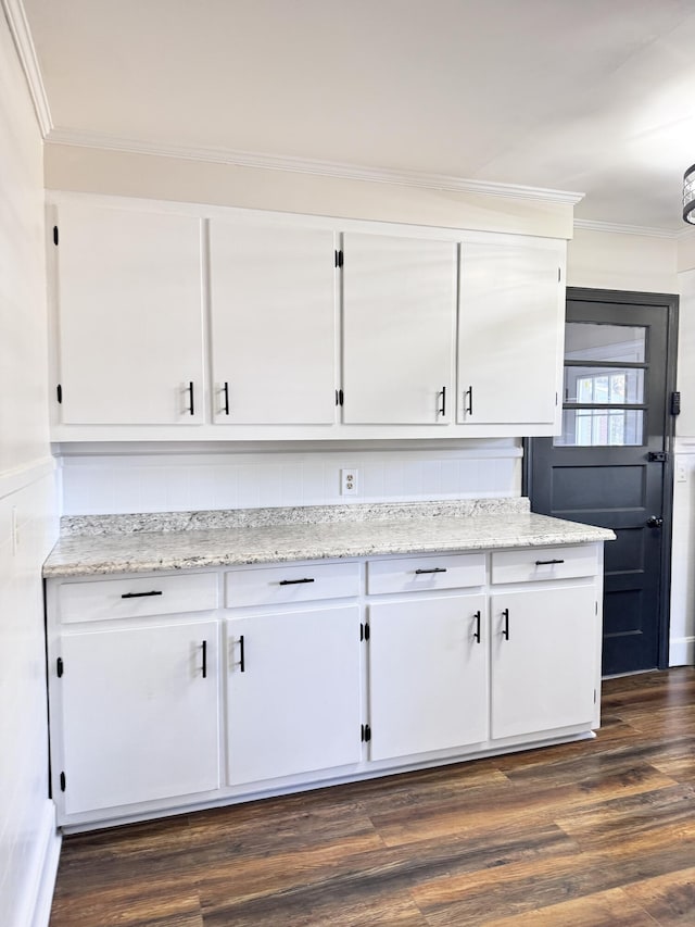 kitchen with light stone countertops, dark hardwood / wood-style flooring, white cabinetry, and ornamental molding