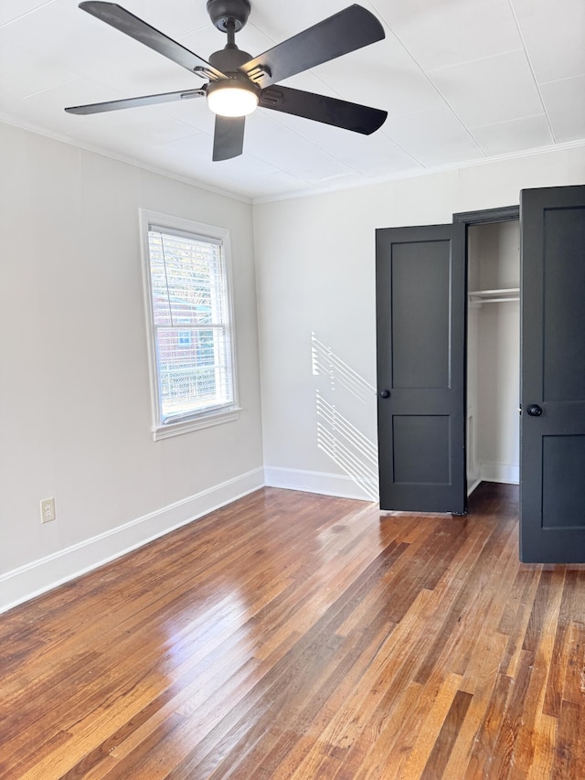 unfurnished bedroom with ceiling fan, dark hardwood / wood-style flooring, crown molding, and a closet