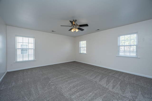 unfurnished room featuring a ceiling fan, visible vents, dark carpet, and baseboards