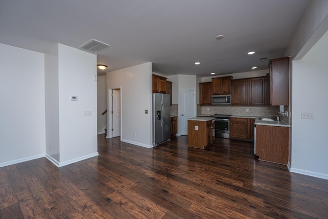 kitchen with stainless steel appliances, dark wood-type flooring, a sink, a kitchen island, and tasteful backsplash