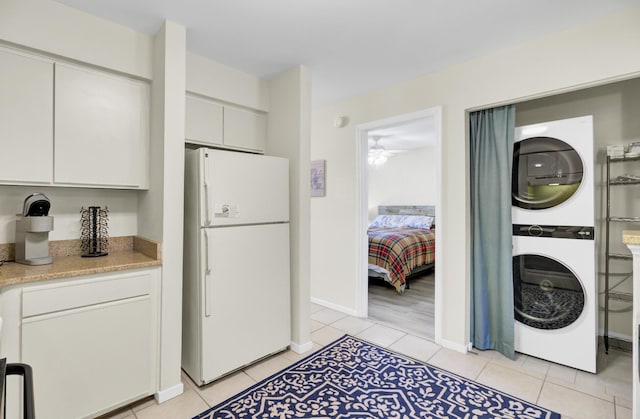 kitchen featuring light tile patterned floors, baseboards, freestanding refrigerator, white cabinetry, and stacked washer / dryer