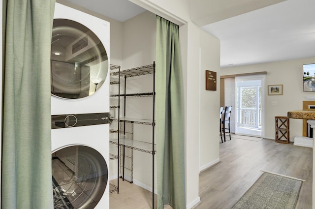 clothes washing area with laundry area, stacked washing maching and dryer, baseboards, and wood finished floors