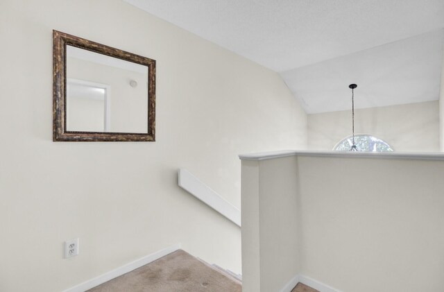 hall with an upstairs landing, vaulted ceiling, baseboards, and carpet floors