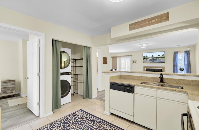 kitchen with stacked washer and clothes dryer, light tile patterned flooring, stove, white dishwasher, and a sink