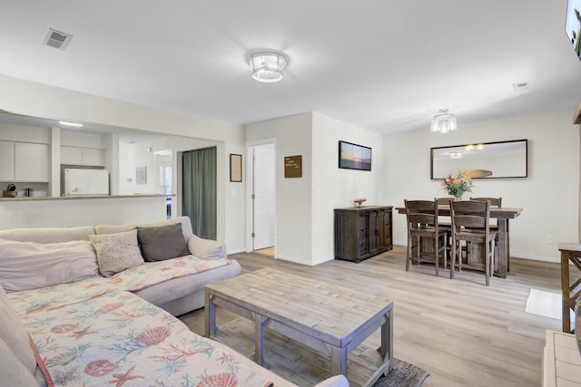 living area with light wood-type flooring, visible vents, and baseboards