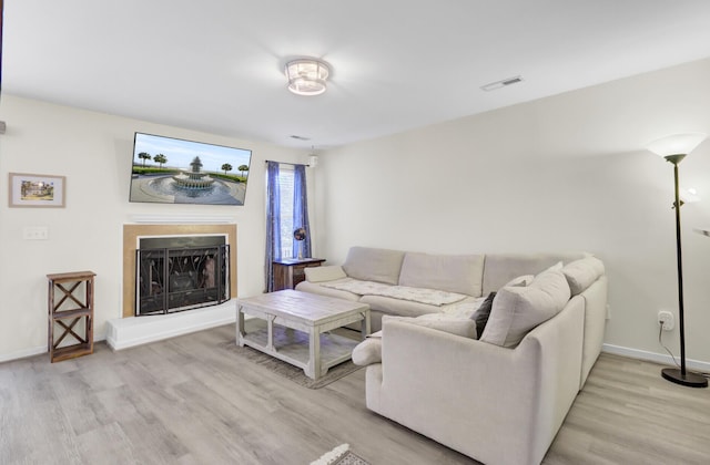 living area featuring light wood-style floors, a fireplace with raised hearth, visible vents, and baseboards