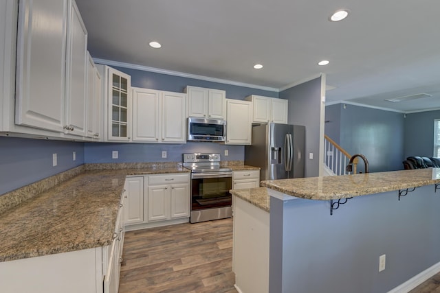 5105 Parrum Ct, Summerville, SC 29485 - kitchen with appliances with stainless steel finishes, ornamental molding, a kitchen breakfast bar, wood finished floors, and white cabinets
