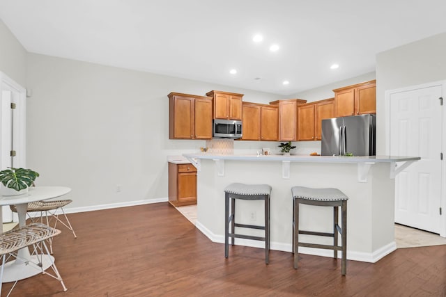 kitchen with stainless steel appliances, a kitchen bar, light countertops, wood finished floors, and baseboards