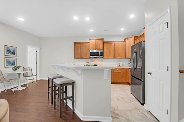 kitchen featuring recessed lighting, light countertops, appliances with stainless steel finishes, a kitchen island, and a kitchen breakfast bar