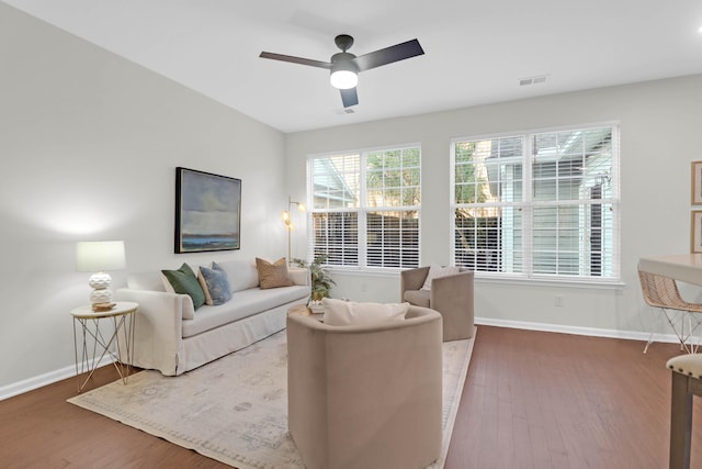 living area with ceiling fan, wood finished floors, visible vents, and baseboards