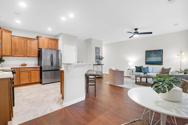 kitchen featuring a ceiling fan, light wood-style flooring, appliances with stainless steel finishes, a breakfast bar, and light countertops