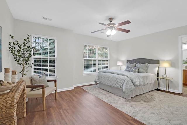 bedroom featuring a ceiling fan, visible vents, baseboards, and wood finished floors