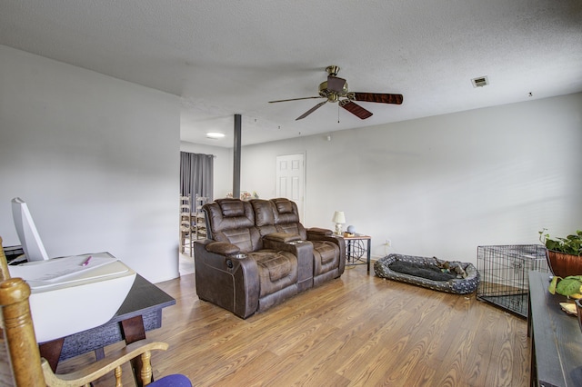 living room featuring ceiling fan, light hardwood / wood-style flooring, and a textured ceiling