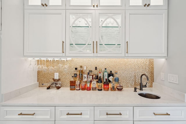 bar featuring white cabinets, backsplash, light stone counters, and sink