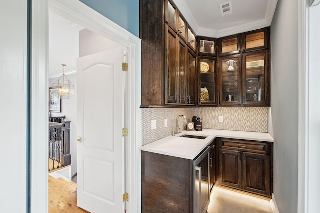 bar with dark brown cabinetry, sink, hanging light fixtures, and light hardwood / wood-style flooring