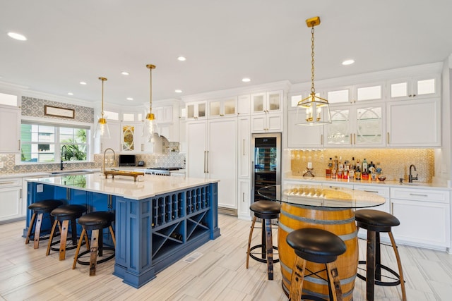 kitchen with white cabinets, a center island with sink, hanging light fixtures, and ornamental molding