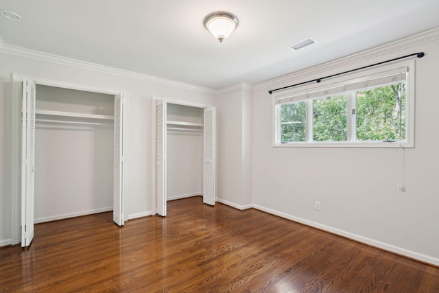 unfurnished bedroom with ornamental molding, dark hardwood / wood-style flooring, and multiple closets