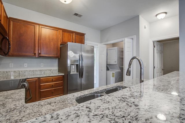 116 Venezia Ct, Ladson, SC 29456 - kitchen featuring stainless steel refrigerator with ice dispenser, stacked washer / dryer, light stone counters, a sink, and brown cabinetry