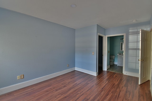 unfurnished bedroom featuring ensuite bathroom and dark hardwood / wood-style flooring